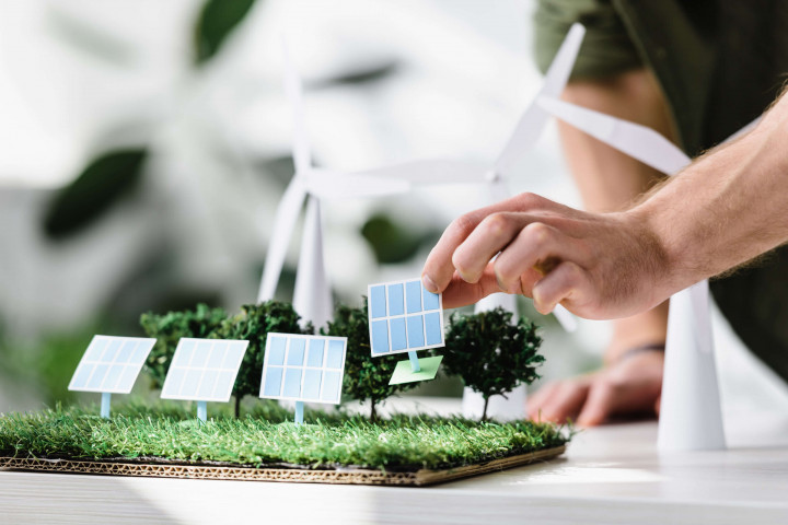 Hand setzt Miniatur-Solarpaneel in Modelllandschaft mit Windrädern – Konzept für nachhaltige Energie