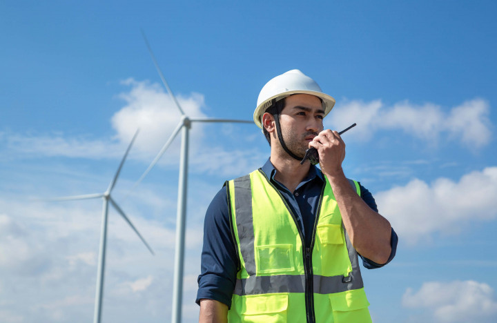 Techniker mit Funkgerät und Schutzweste vor Windkraftanlagen – Kommunikation auf der Baustelle
