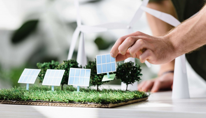 Hand setzt Miniatur-Solarpaneel in Modelllandschaft mit Windrädern – Konzept für nachhaltige Energie